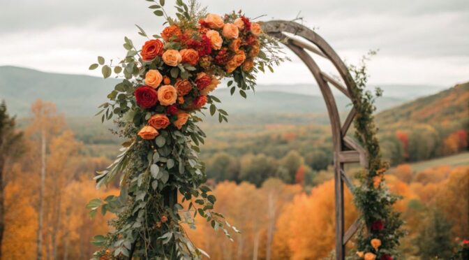 A fall wedding floral arch with sage green eucalyptus and burnt orange ranunculus under autumn leaves
