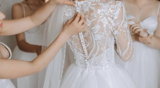 Bride examining intricate lace details on wedding gown in boutique mirror