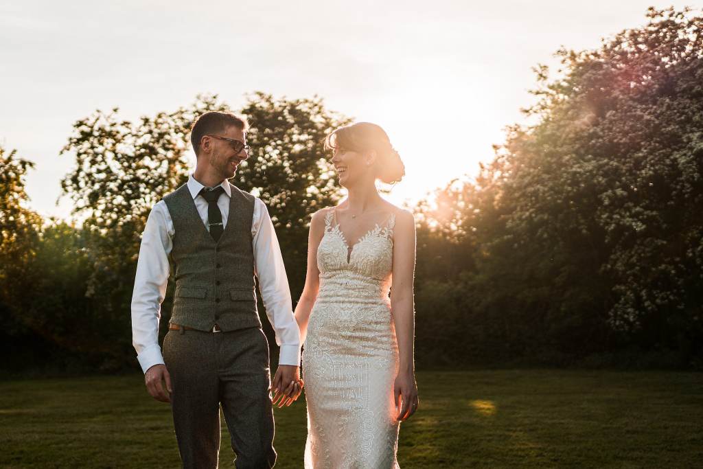 Happy bride in fitted lace dress walking outdoors with venue in background